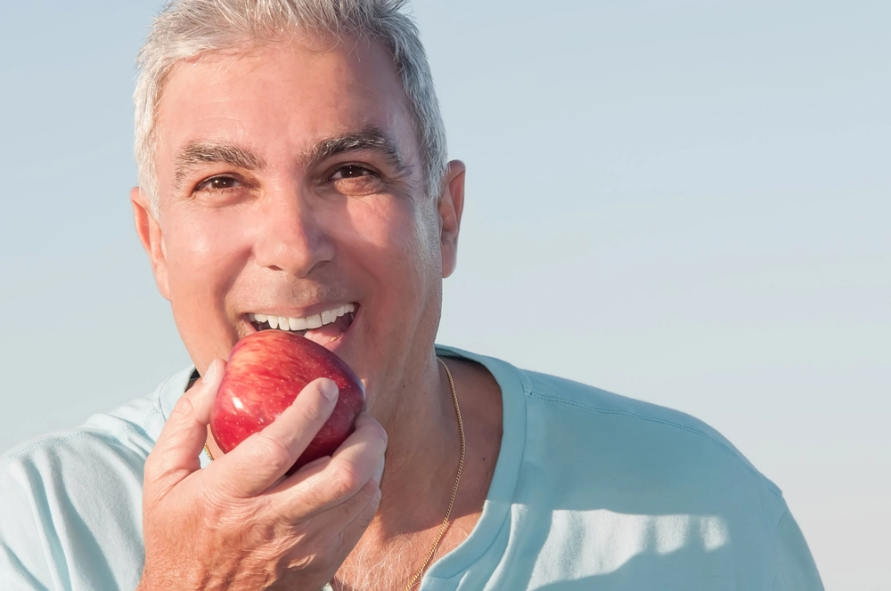 older man smiling with an apple in hand