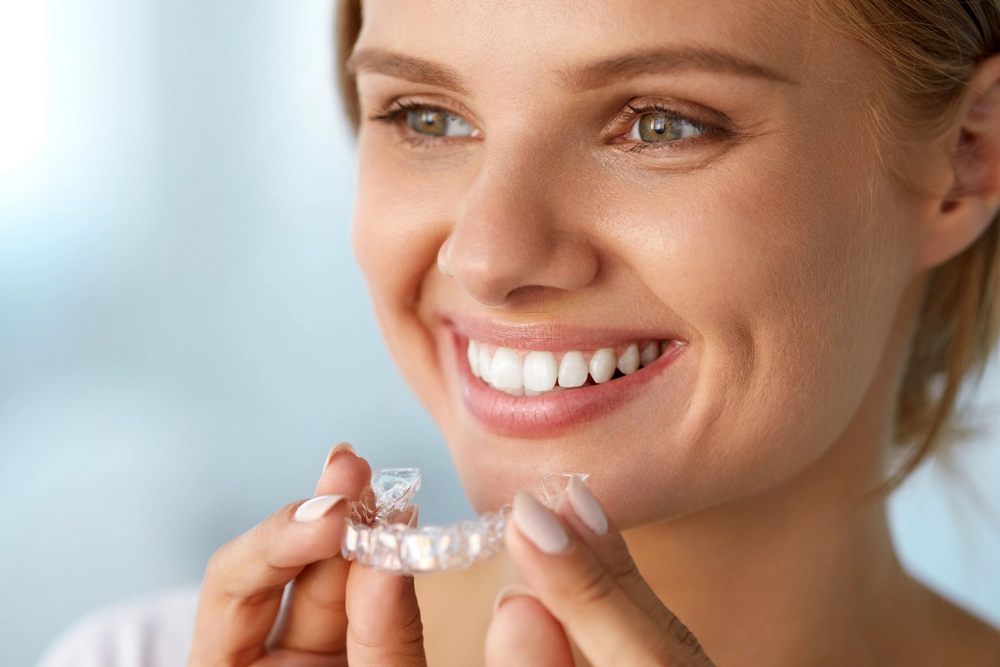 close-up of smiling woman holding clear braces mouthpiece
